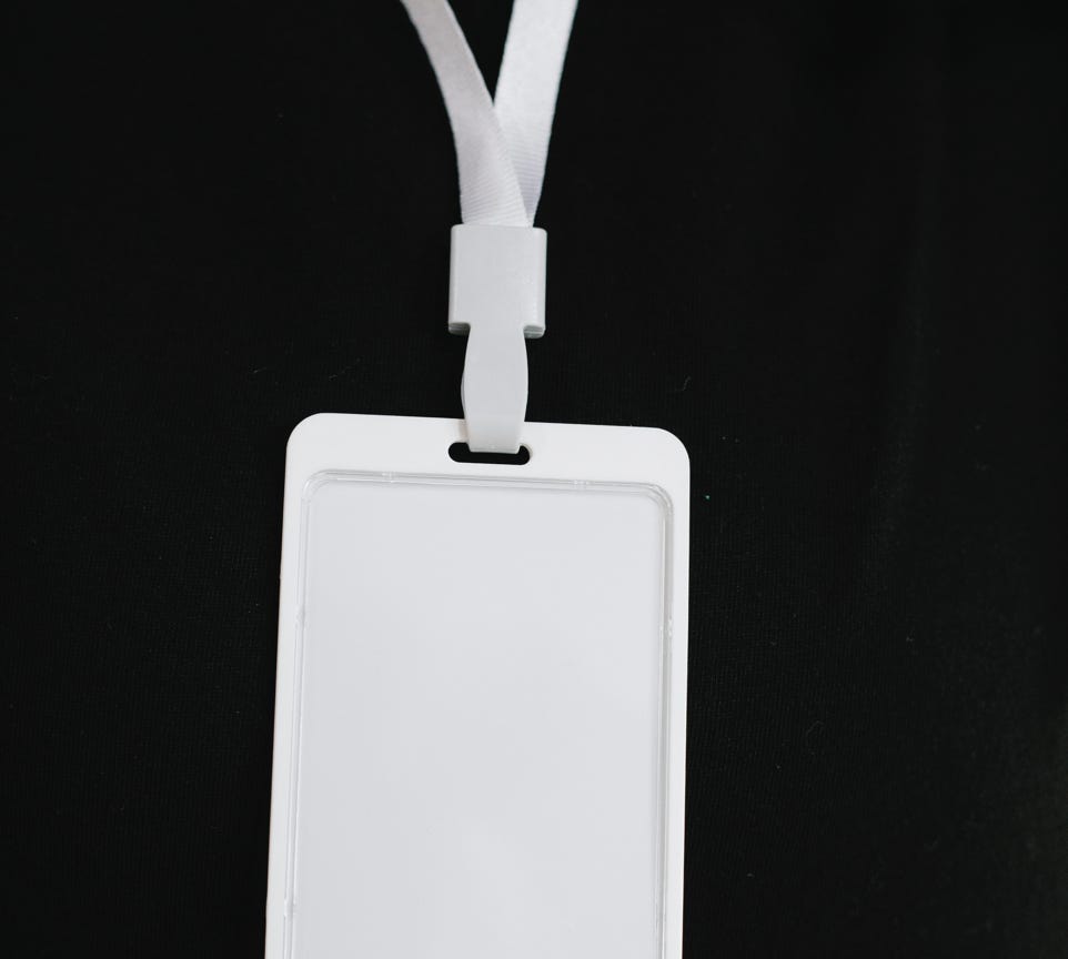 Plastic name tag with white ribbon and blank paper hanging on black background